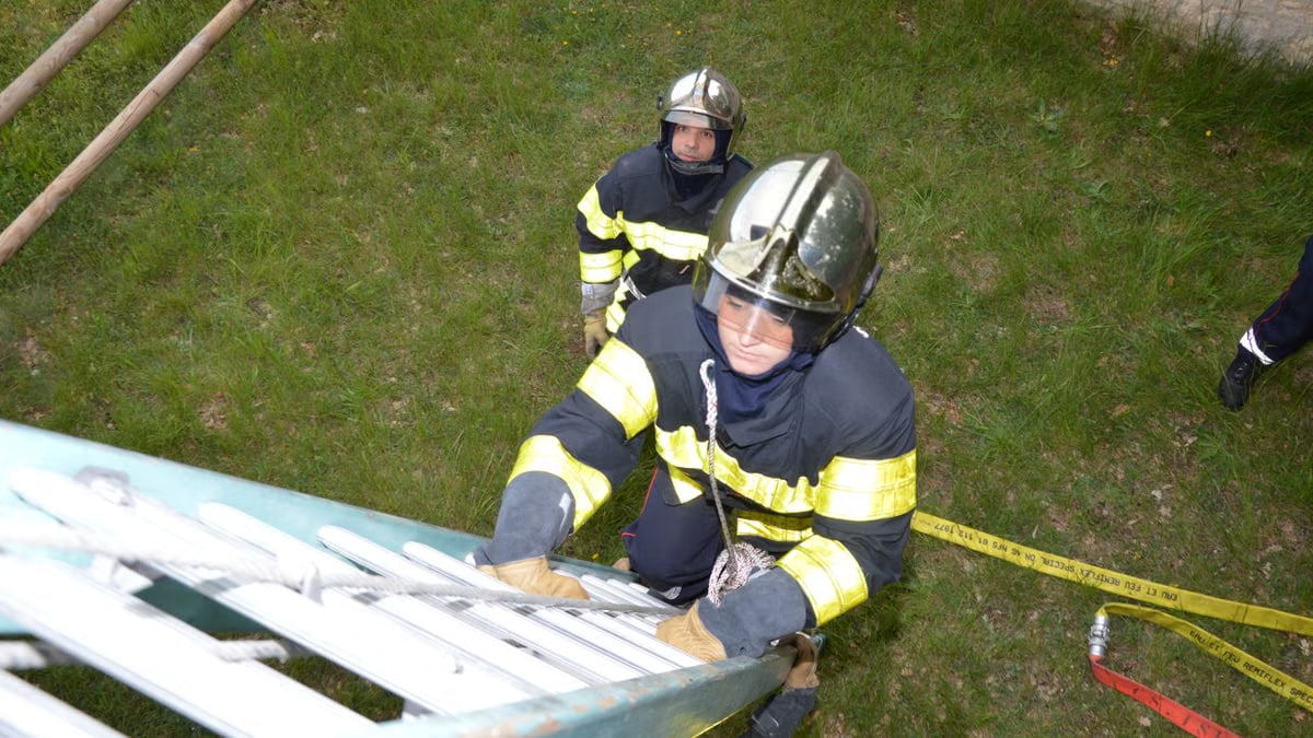 A firefighter climbs a ladder during a training exercise, with safety gear and protective clothing.